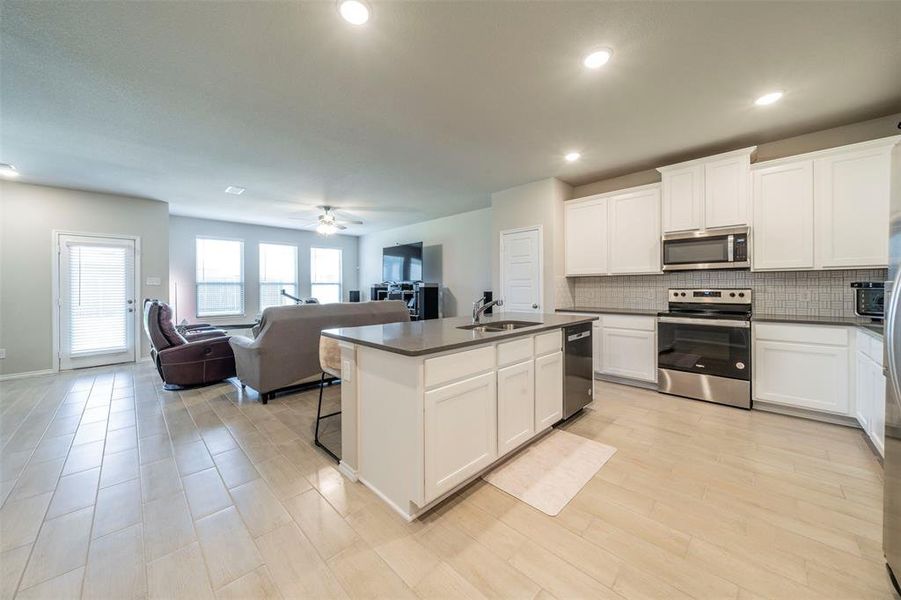 Kitchen with a kitchen island with sink, sink, ceiling fan, appliances with stainless steel finishes, and white cabinets