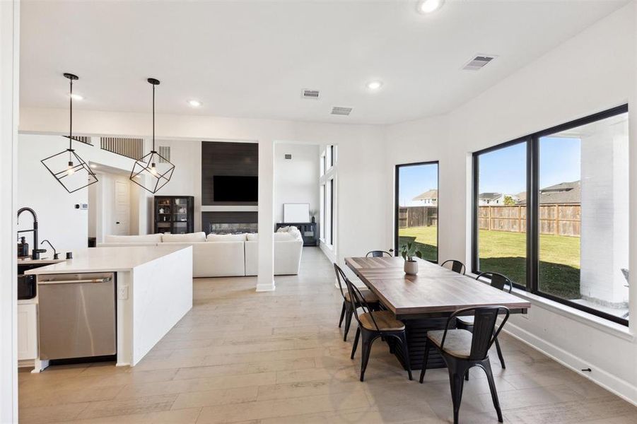 The sleek kitchen features stainless steel appliances, an expansive central island, and a dining space with room for a large table. Natural light floods the room through ample windows, and the area flows seamlessly into a comfortable living room.