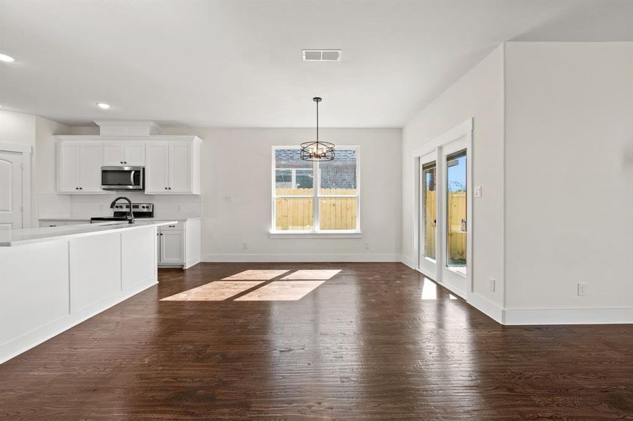 Kitchen featuring dark hardwood / wood-style flooring, pendant lighting, stainless steel appliances, white cabinetry, and a chandelier