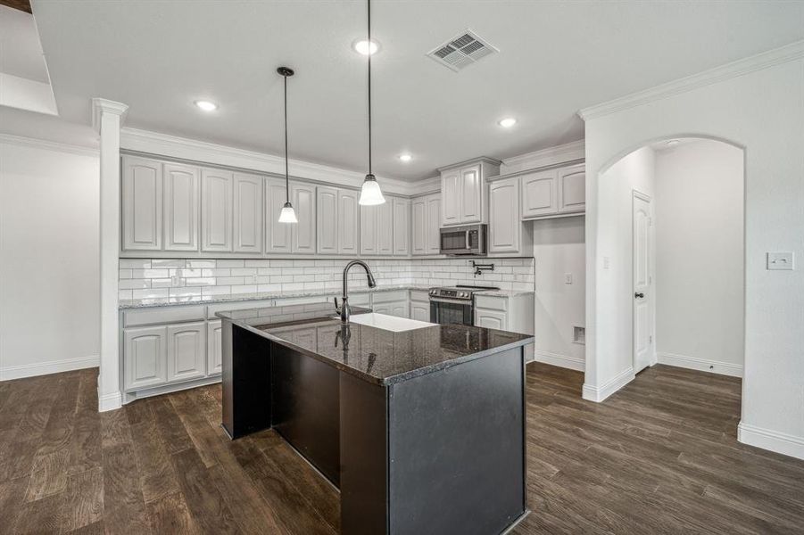 Kitchen featuring appliances with stainless steel finishes, dark stone counters, a center island with sink, decorative light fixtures, and dark hardwood / wood-style floors