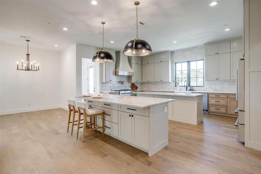 Kitchen featuring a spacious island, pendant lighting, light stone countertops, and premium range hood