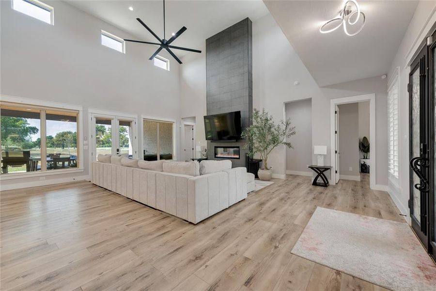 Living room with light hardwood / wood-style floors, ceiling fan with notable chandelier, a high ceiling, and a large fireplace