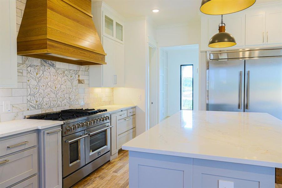 Kitchen with custom exhaust hood, tasteful backsplash, light wood-type flooring, a center island, and high end appliances