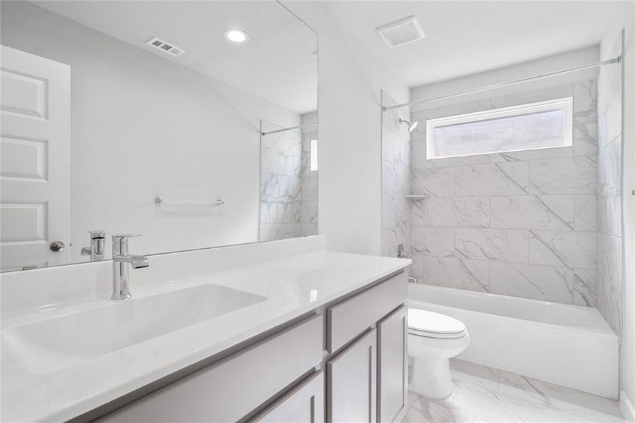 Secondary bath features tile flooring, bath/shower combo with tile surround, stained wood cabinets, beautiful light countertops, mirror, sleek fixtures and modern finishes.