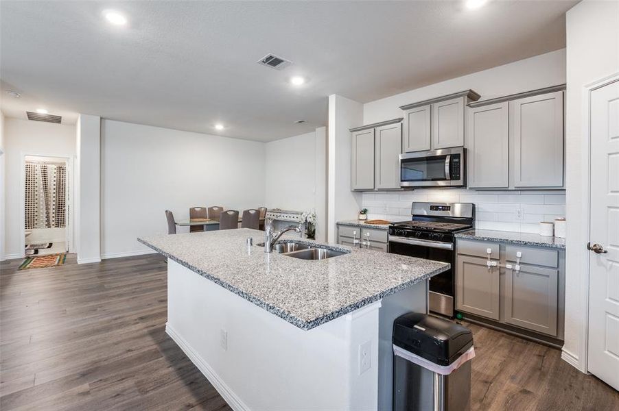 Kitchen with dark hardwood / wood-style floors, an island with sink, sink, appliances with stainless steel finishes, and light stone counters