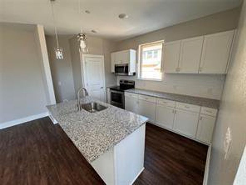 Kitchen featuring white cabinets, a center island with sink, appliances with stainless steel finishes, and decorative light fixtures