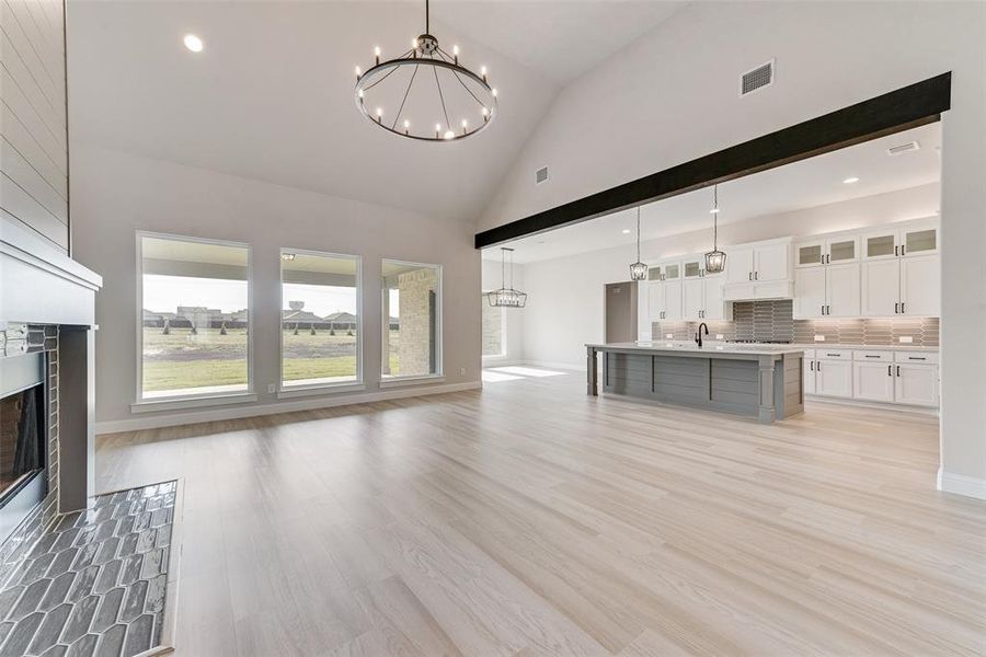 Unfurnished living room with light wood-type flooring, an inviting chandelier, sink, and high vaulted ceiling