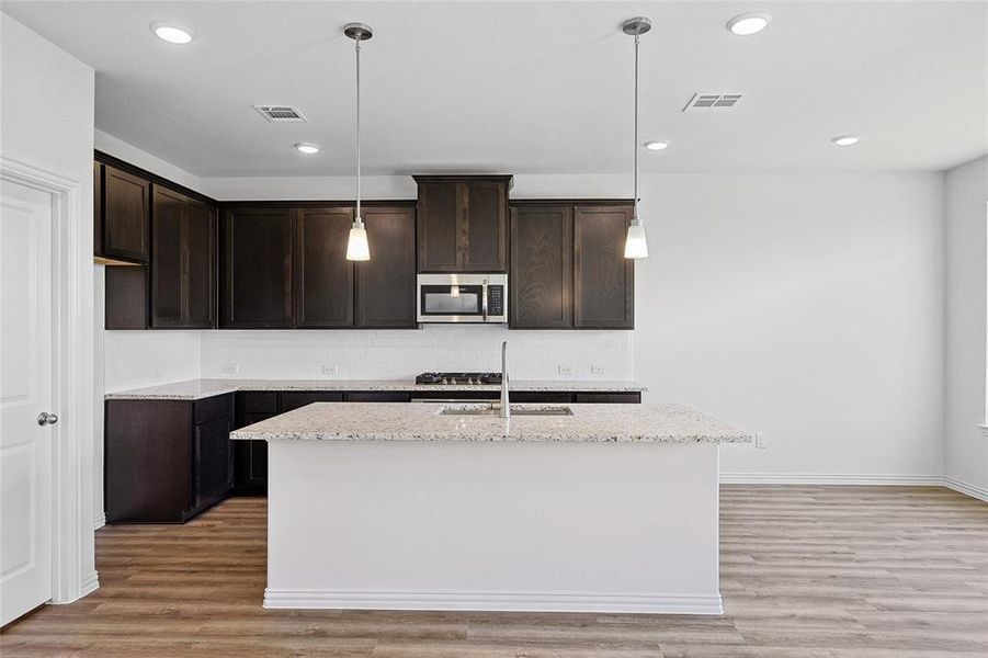 Kitchen featuring a center island with sink, hanging light fixtures, light hardwood / wood-style floors, and tasteful backsplash