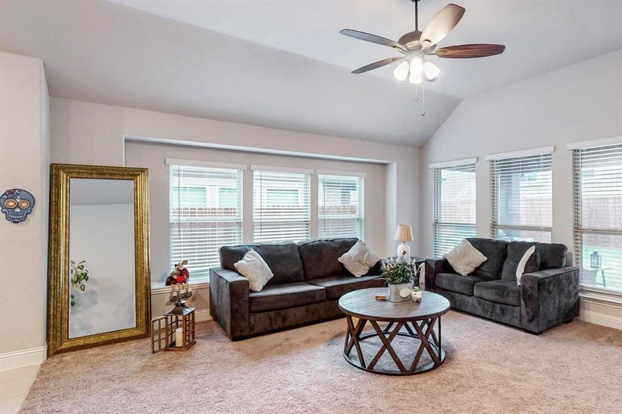 Carpeted living room featuring ceiling fan and vaulted ceiling