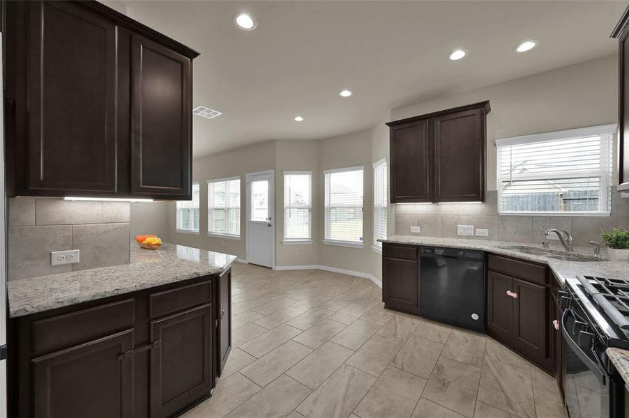 This is a spacious modern kitchen featuring dark wood cabinets, granite countertops, plenty of counterspace, and tiled flooring. Natural light floods the room through multiple windows.