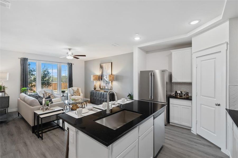 Kitchen with white cabinetry, sink, wood-type flooring, ceiling fan, and a kitchen island with sink