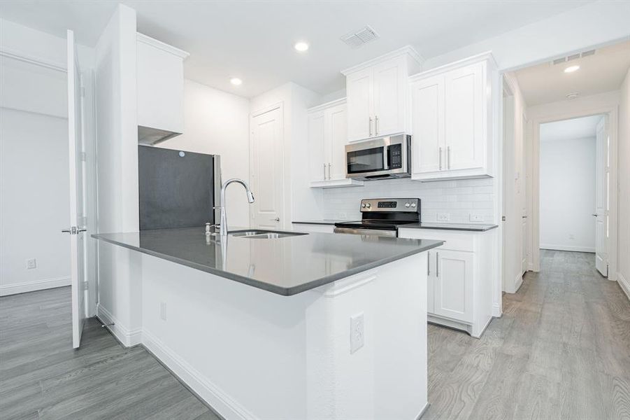 Kitchen with sink, light hardwood / wood-style floors, white cabinets, and appliances with stainless steel finishes