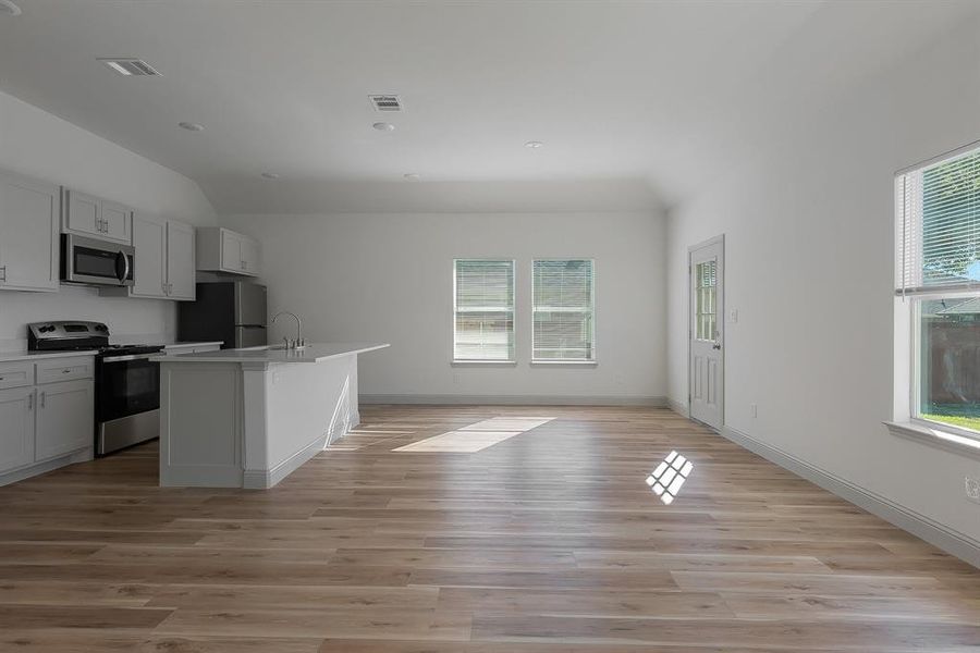 Kitchen featuring appliances with stainless steel finishes, light hardwood / wood-style floors, a kitchen island with sink, and lofted ceiling