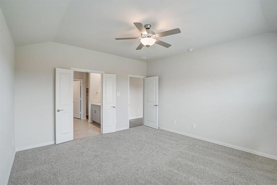 Primary suite. Bedroom with light colored carpet, vaulted ceiling, ensuite bath, and ceiling fan