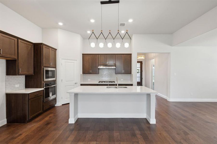 Kitchen featuring dark brown cabinets, stainless steel appliances, dark hardwood / wood-style flooring, and a center island with sink