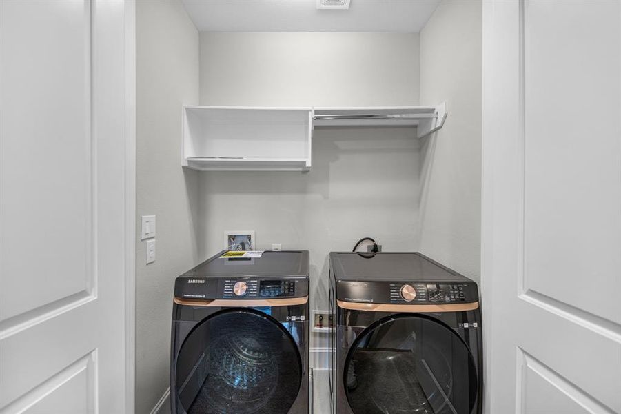 The spacious laundry room offers plenty of room for full-size appliances, complete with connections for both gas and electric dryers. Thoughtfully designed, it features overhead shelving for easy storage of laundry essentials and a convenient hanging rod for drying garments or organizing clothes straight out of the wash.