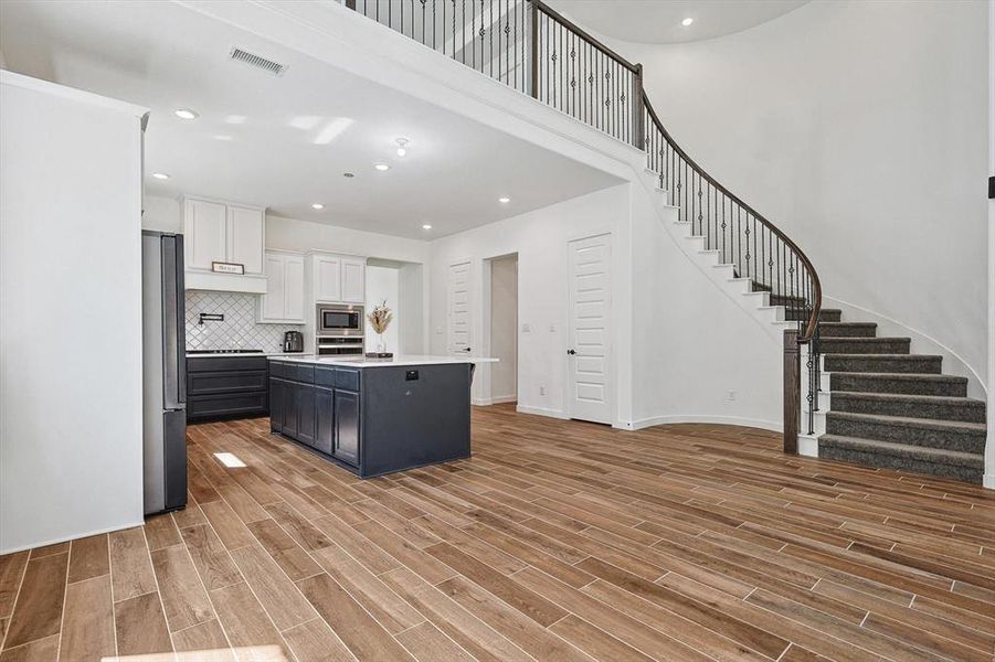 Kitchen with a kitchen island, decorative backsplash, stainless steel appliances, white cabinets, and light hardwood / wood-style floors