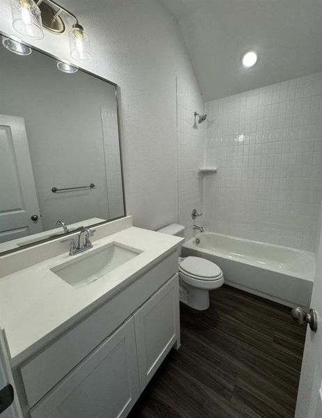 Full bathroom with vanity, hardwood / wood-style flooring, tiled shower / bath, and toilet