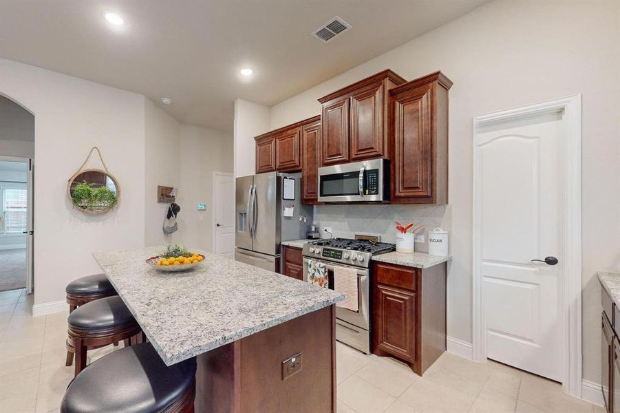 Kitchen with light stone counters, stainless steel appliances, a kitchen island, light tile patterned floors, and a breakfast bar area