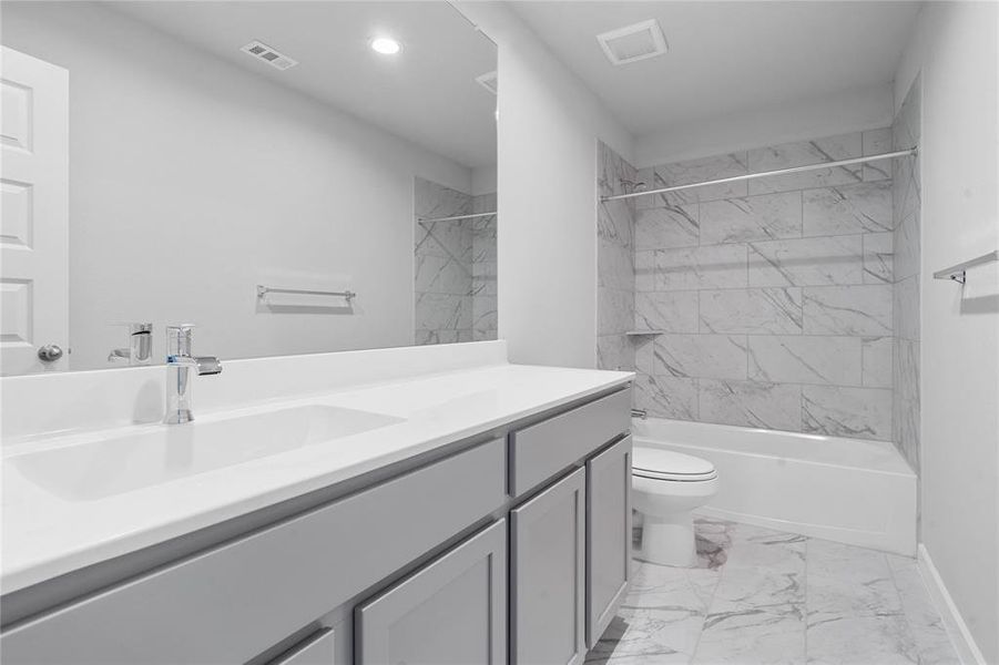 Secondary bath features tile flooring, bath/shower combo with tile surround, stained cabinets, beautiful light countertops, mirror, sleek fixtures and modern finishes.