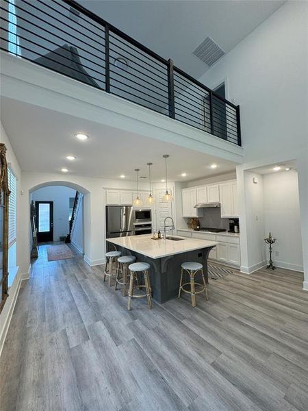 Kitchen with appliances with stainless steel finishes, light wood-type flooring, hanging light fixtures, a large island, and white cabinets