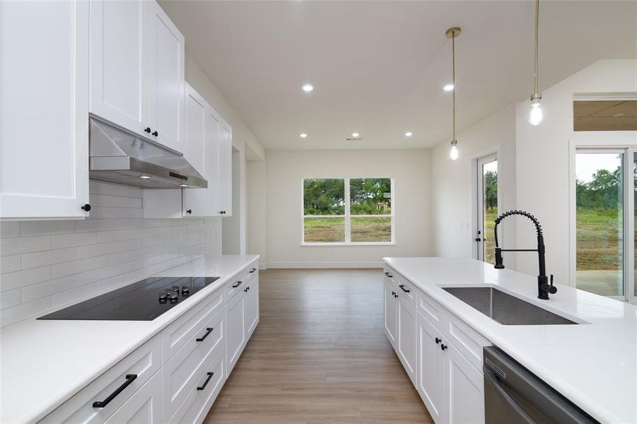 Kitchen featuring black electric cooktop, white cabinetry, light hardwood / wood-style flooring, decorative light fixtures, and sink