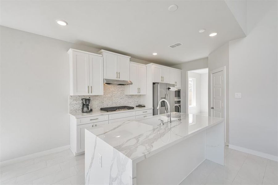 Modern kitchen featuring white cabinetry, stainless steel appliances, and elegant marble countertops with a spacious island.