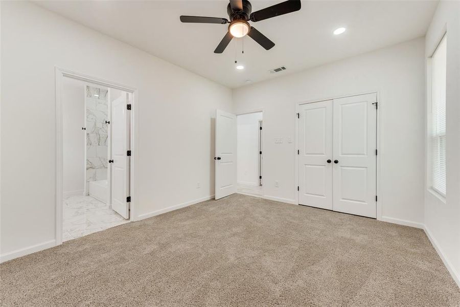 Unfurnished bedroom featuring light colored carpet, ensuite bathroom, ceiling fan, and a closet