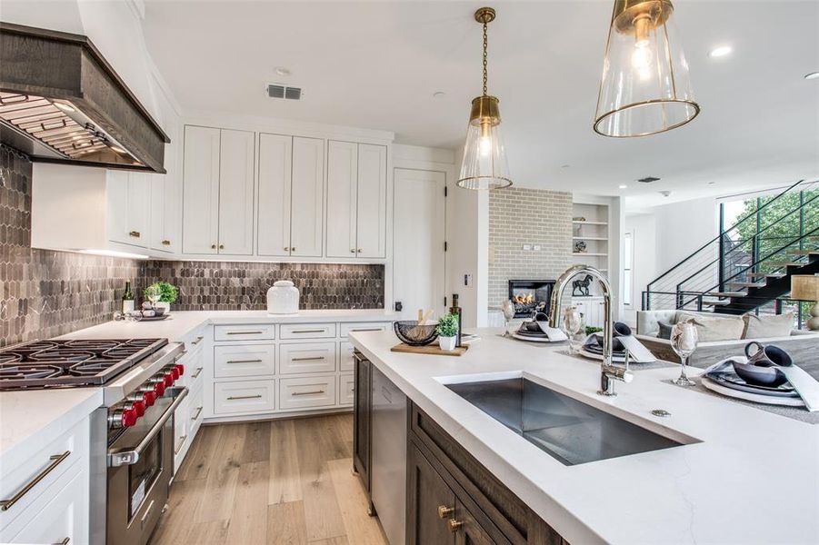 Kitchen featuring sink, white cabinetry, hanging light fixtures, custom range hood, and appliances with stainless steel finishes