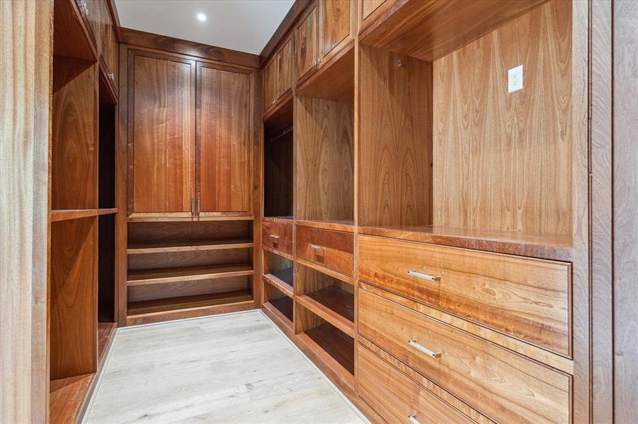 This handsome dark wood primary closet exudes a country club flair, offering a refined and sophisticated storage space for your wardrobe. Its rich finishes and thoughtful design create an inviting atmosphere that makes getting dressed a luxurious experience.