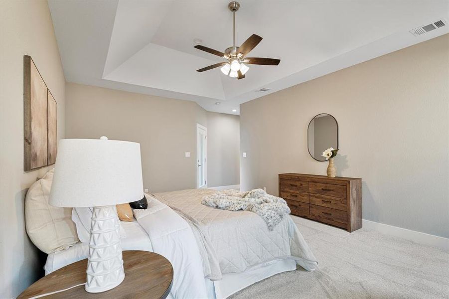 Bedroom with ceiling fan, light colored carpet, and a tray ceiling