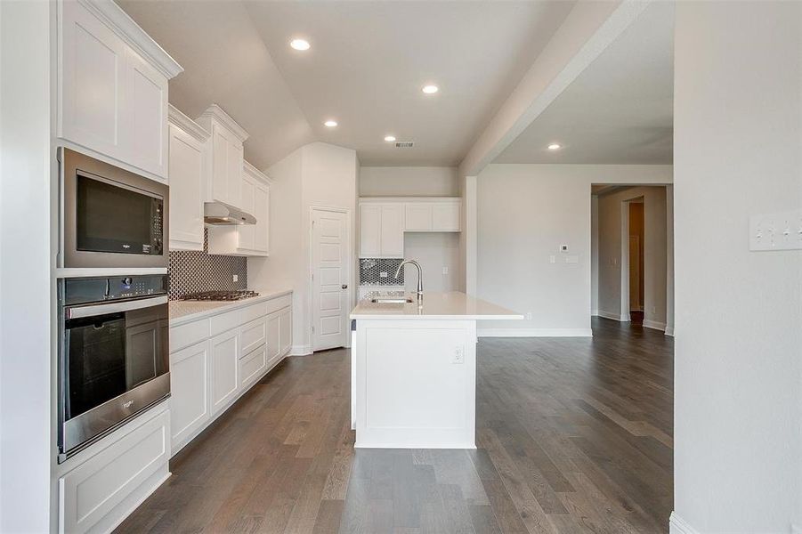 Kitchen featuring an island with sink, white cabinets, decorative backsplash, stainless steel appliances, and dark hardwood / wood-style flooring