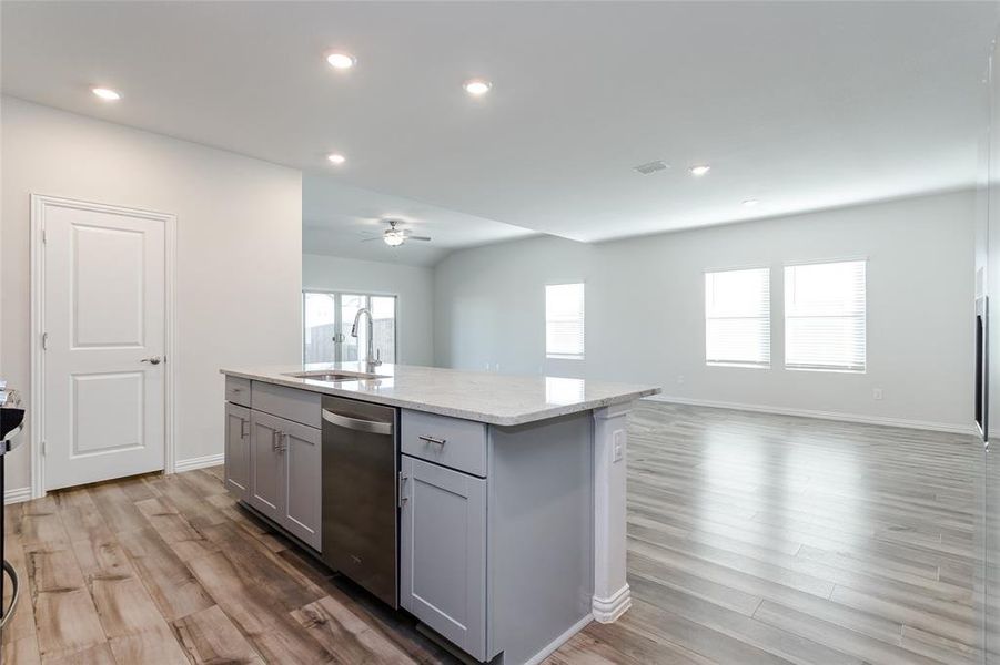 Kitchen featuring sink, stainless steel dishwasher, an island with sink, gray cabinetry, and light wood-type flooring