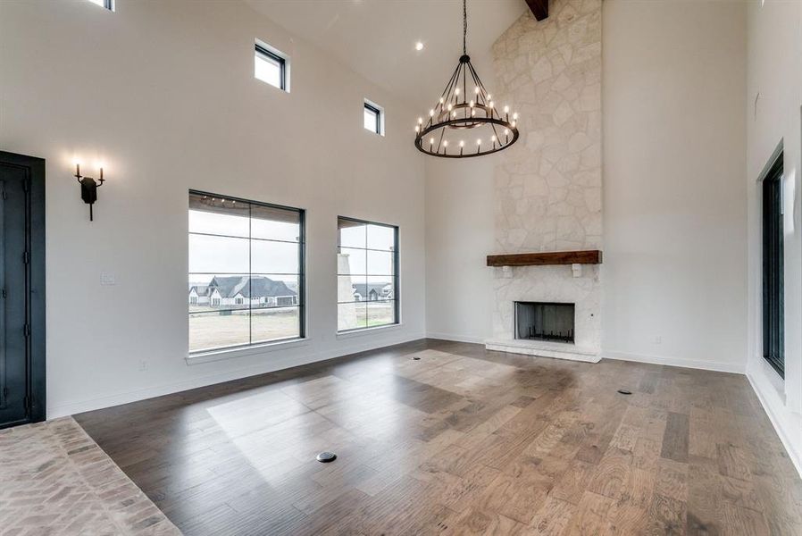 Unfurnished living room featuring a notable chandelier, hardwood / wood-style flooring, high vaulted ceiling, and a stone fireplace