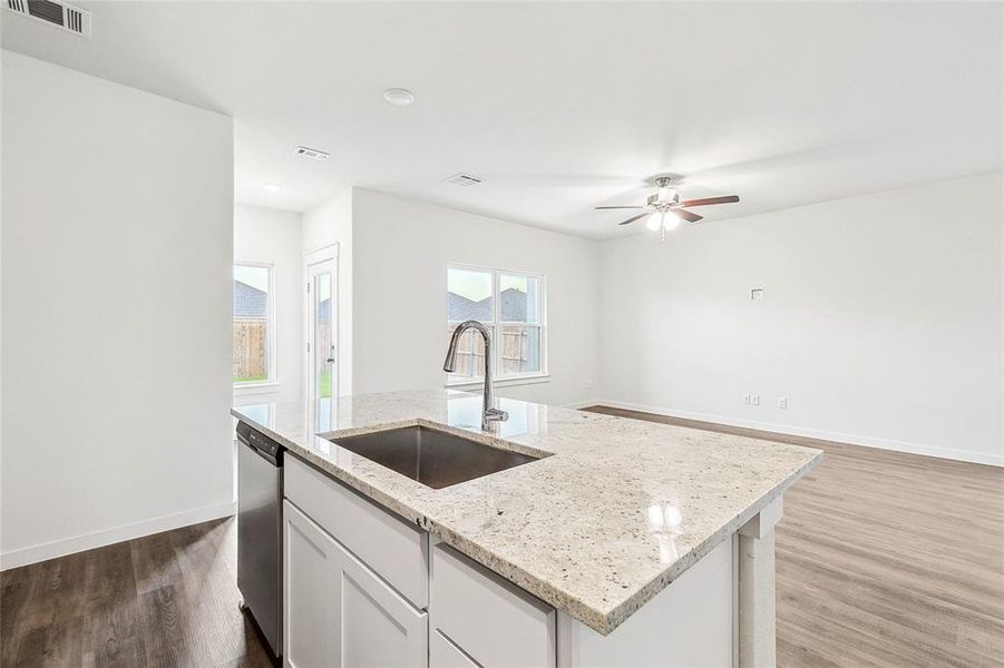 Kitchen featuring wood-type flooring, ceiling fan, sink, light stone countertops, and a kitchen island with sink