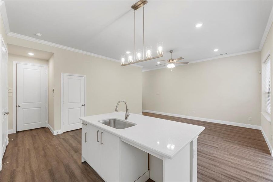 Kitchen featuring sink, pendant lighting, ornamental molding, dark hardwood / wood-style floors, and a kitchen island with sink