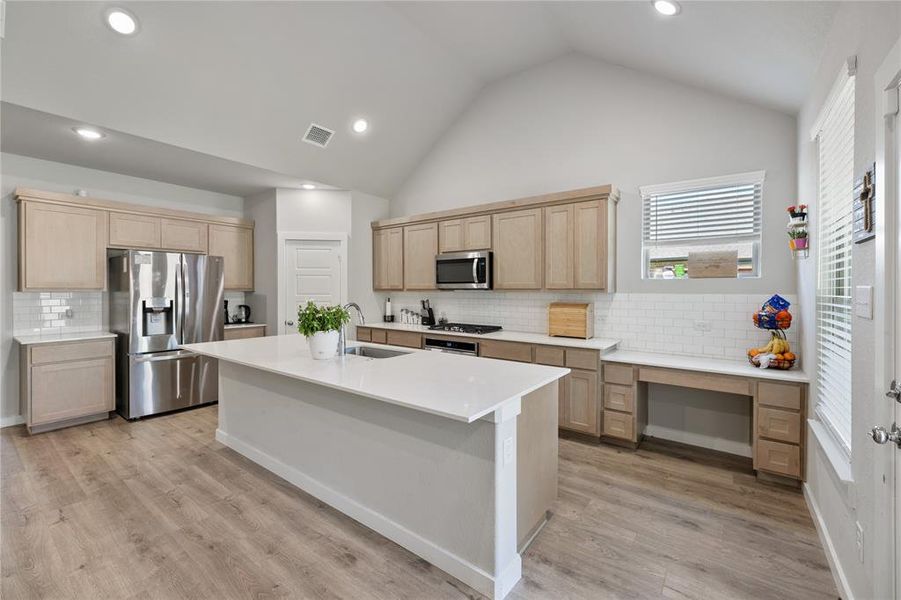 Kitchen with tasteful backsplash, stainless steel appliances, light hardwood / wood-style floors, and an island with sink