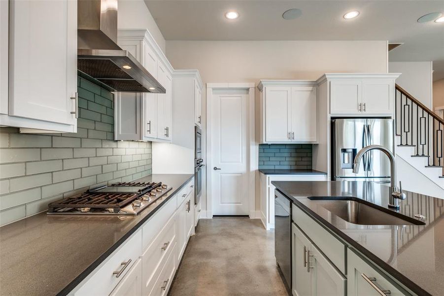 Kitchen with appliances with stainless steel finishes, white cabinets, and wall chimney range hood