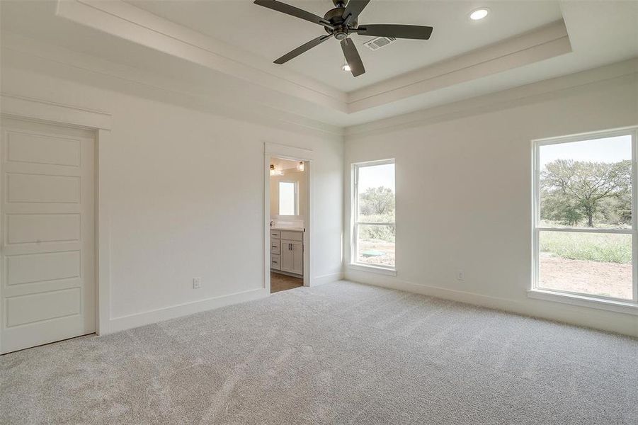 Unfurnished bedroom with carpet floors, ensuite bath, a raised ceiling, and ceiling fan