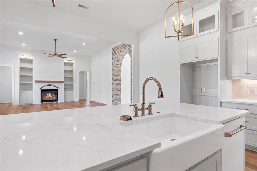 Kitchen featuring light hardwood / wood-style floors, sink, light stone countertops, hanging light fixtures, and white cabinets