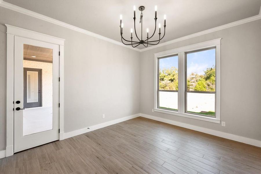 Empty room with ornamental molding, a chandelier, and light wood-type flooring