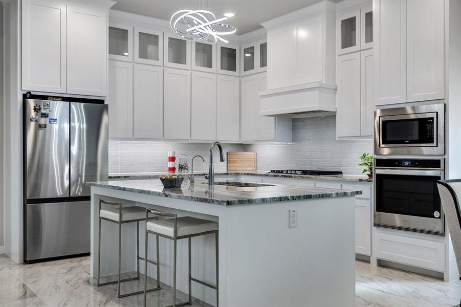 Kitchen featuring appliances with stainless steel finishes, tasteful backsplash, premium range hood, and a kitchen island with sink