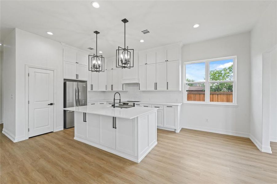 Kitchen featuring an island with sink, light hardwood / wood-style floors, stainless steel fridge, and tasteful backsplash