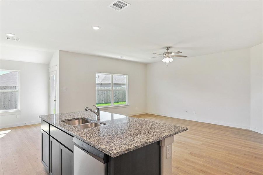 Kitchen with light stone countertops, a kitchen island with sink, sink, light hardwood / wood-style floors, and dishwasher