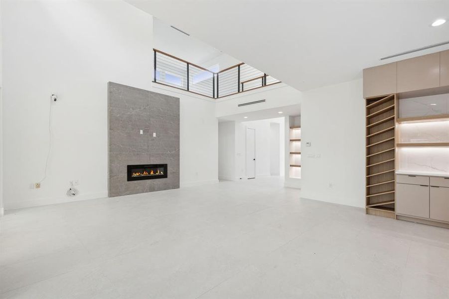 Unfurnished living room featuring a high ceiling, light tile flooring, and a fireplace