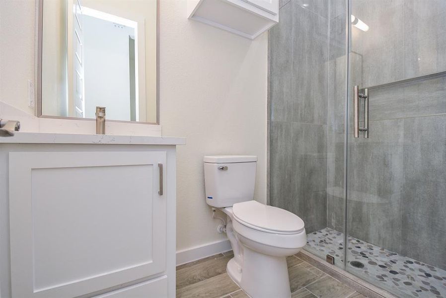 This full bath features quartz countertops, a white storage cabinet, and a standing shower with a glass door.