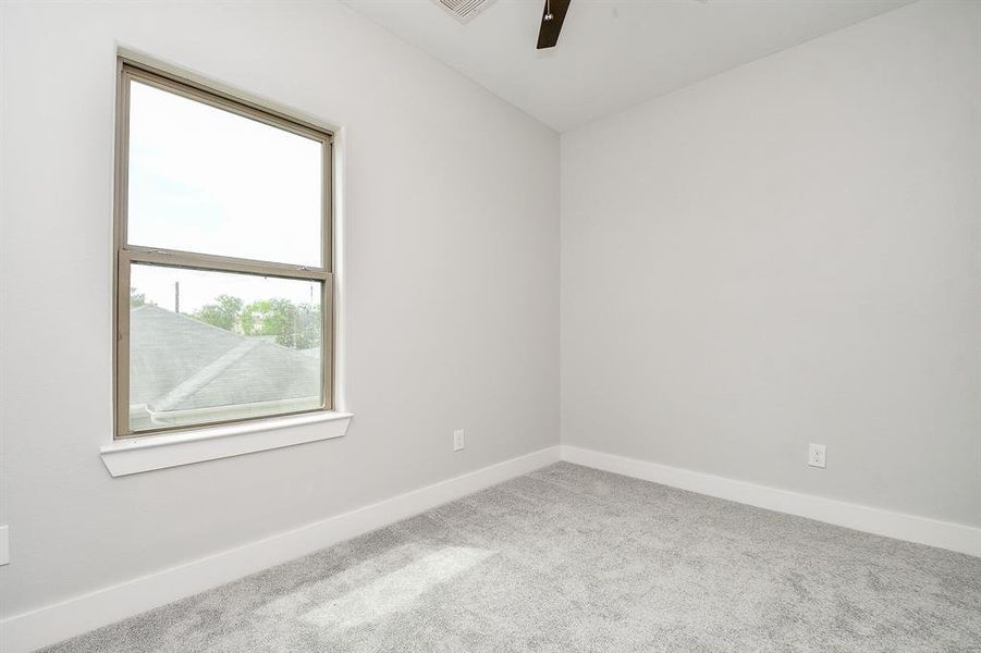 This is a bright, large secondary  bedroom with a large window, plush carpeting, and a modern ceiling fan, offering a clean canvas for personalization.