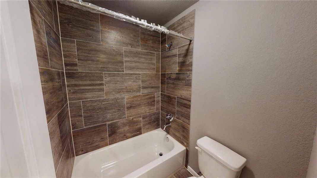 The bathroom showcases a modern shower/tub combo with wood-look tiles, adding a touch of rustic elegance. The design ensures a relaxing bathing experience while enhancing the overall aesthetic of the space. This is a picture of an Elise Floor Plan with another Saratoga Homes.