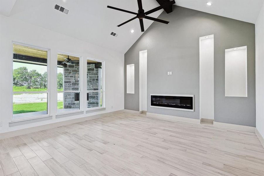 Unfurnished living room featuring beamed ceiling, light hardwood / wood-style flooring, high vaulted ceiling, and ceiling fan