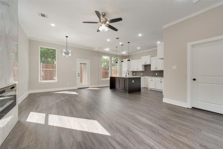 Unfurnished living room featuring sink, ornamental molding, dark hardwood / wood-style floors, and ceiling fan with notable chandelier